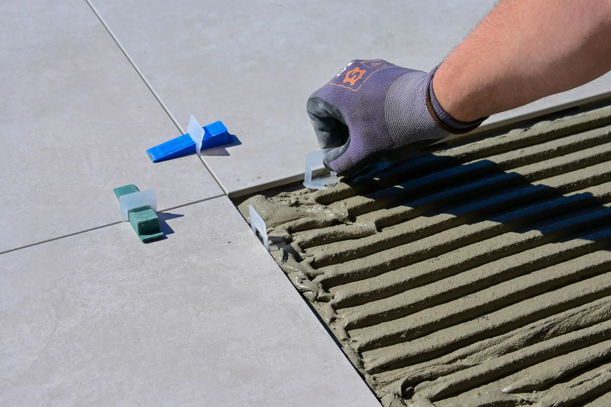Gloved hand setting large format floor tile with levelling clips