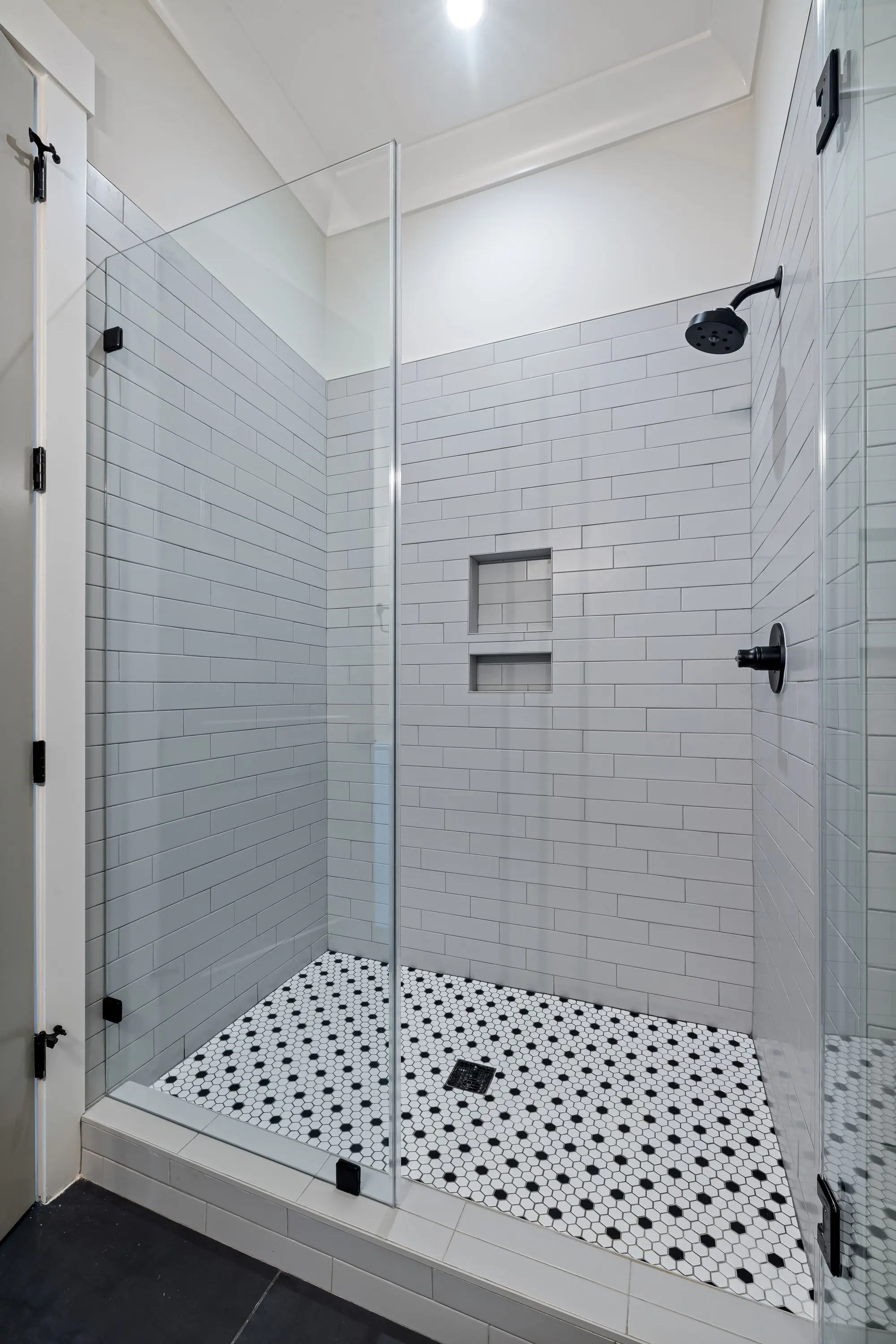 Walk-in shower with white subway tile, a niche and black hardware